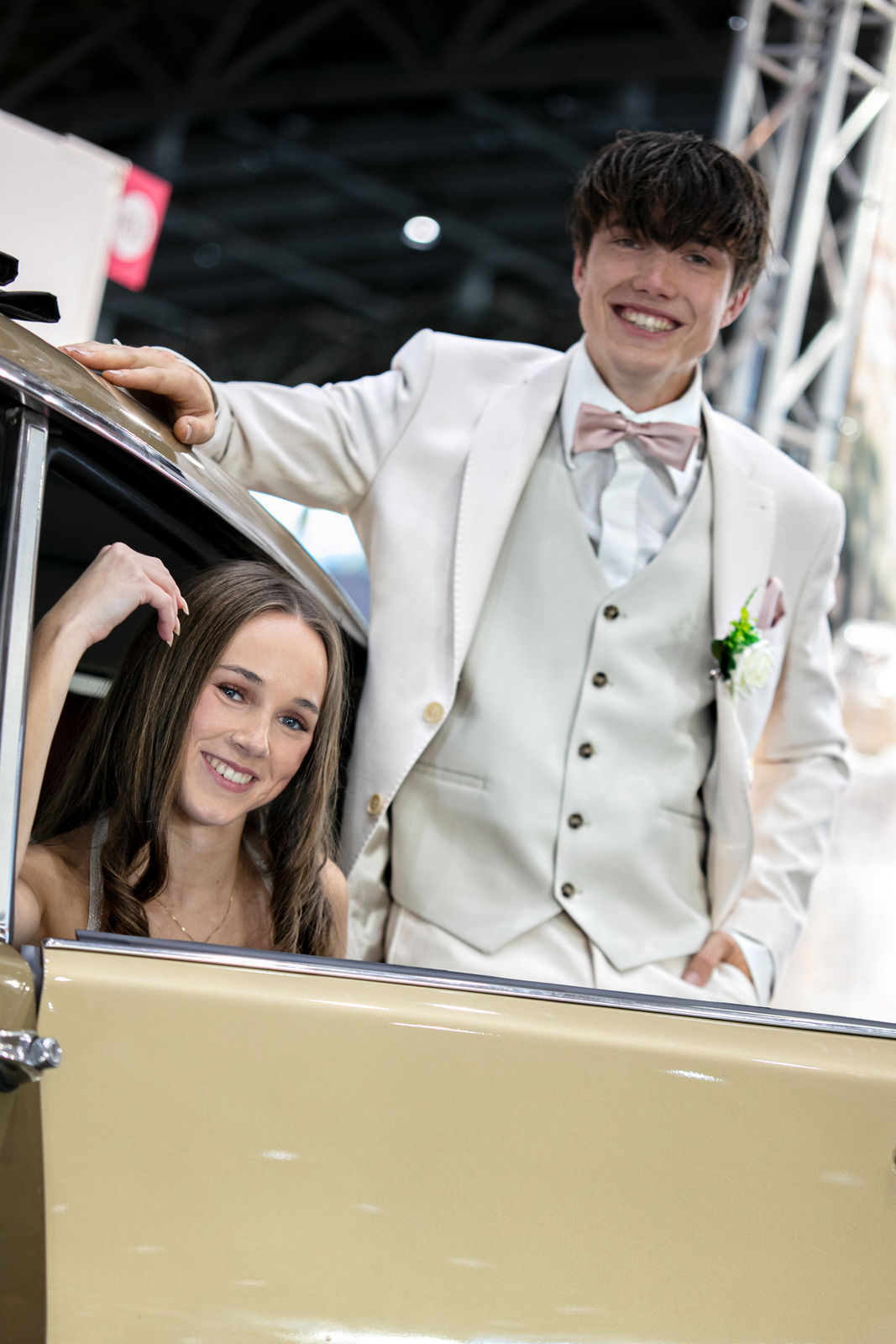 Junge im Anzug und Mädchen im Abendkleid posieren an einem Auto.