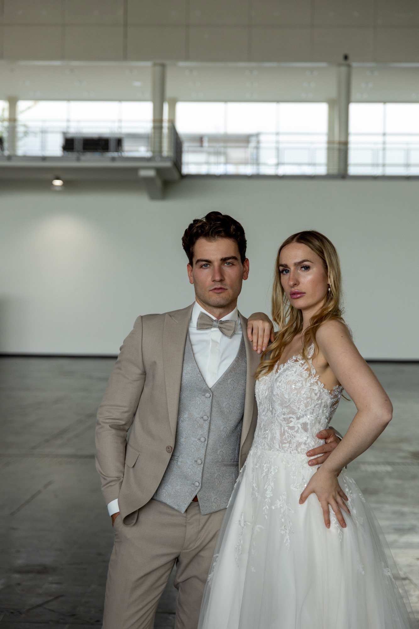 Brautpaar in eleganter Kleidung, posierend vor einem modernen Hintergrund.