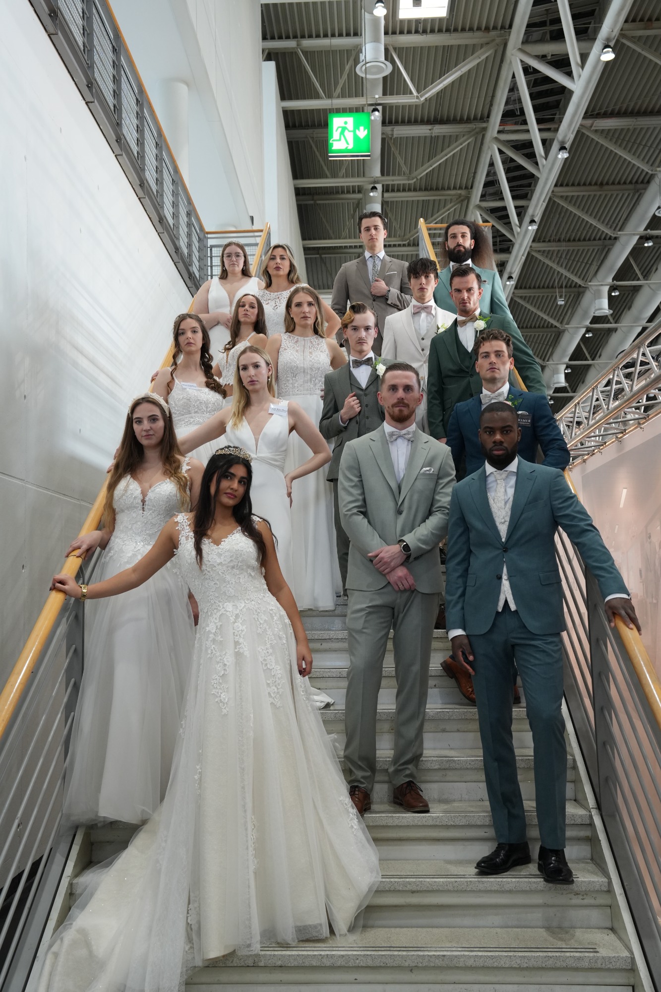 Hochzeitsgesellschaft auf einer Treppe, elegante Kleidung in Weiß und Pastelltönen.