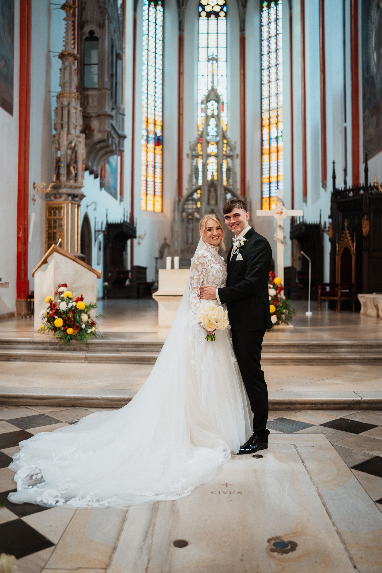 Brautpaar steht glücklich in der Kirche, umgeben von bunten Blumenarrangements.