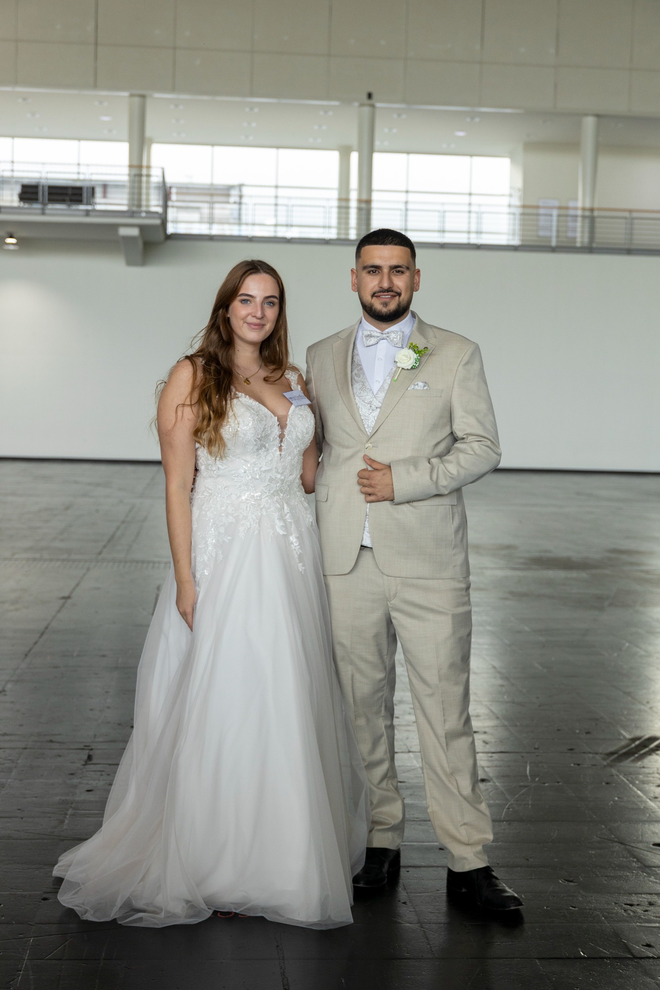 Brautpaar in eleganter Hochzeitskleidung, lächelnd in einem modernen Veranstaltungsraum.