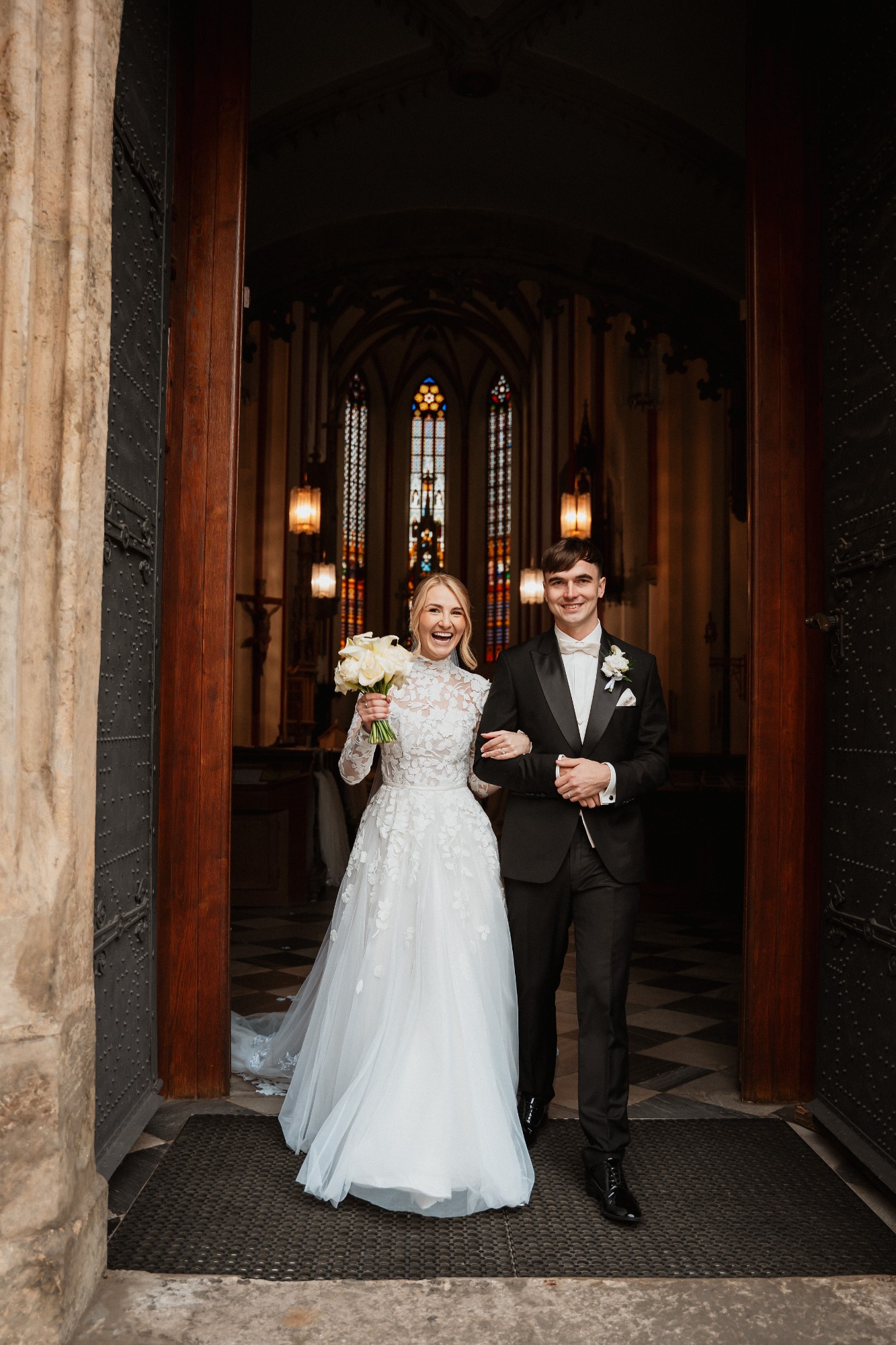 Braut in weißem Kleid und Bräutigam treten glücklich aus der Kirche.