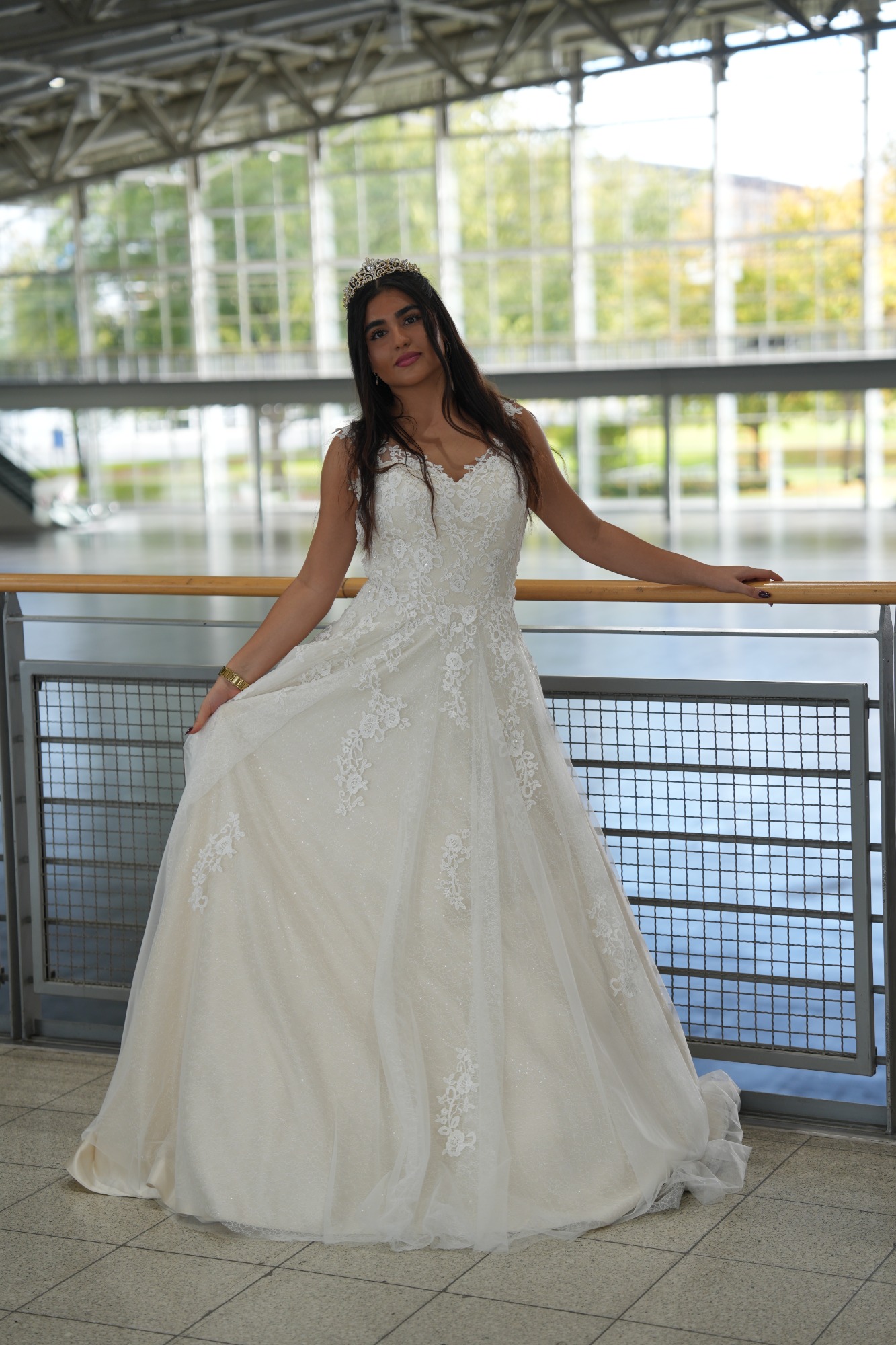 Frau in weißem Brautkleid steht in einem modernen Raum mit großen Fenstern.