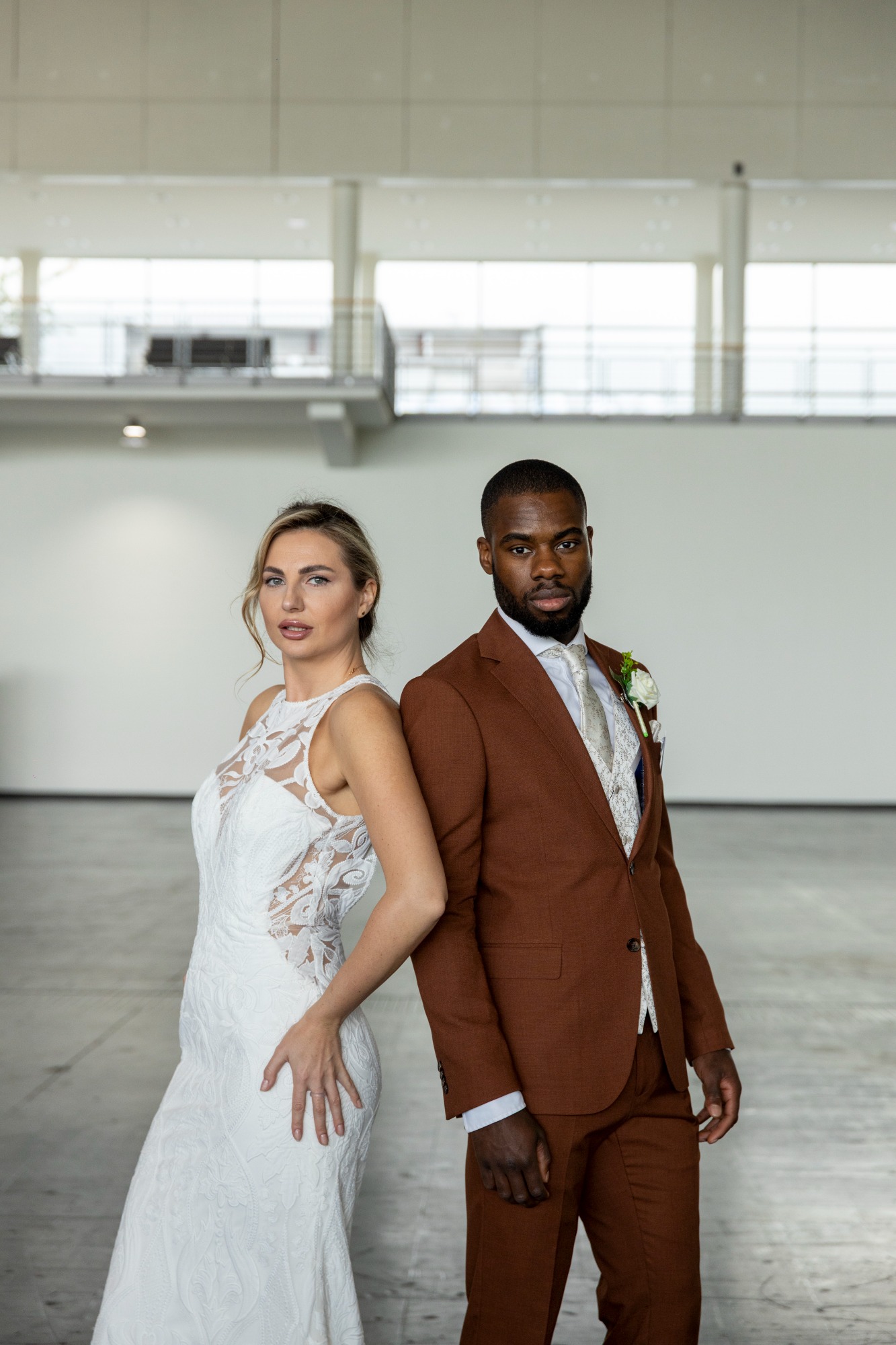 Braut in weißem Kleid und Bräutigam in braunem Anzug stehen nebeneinander in einem modernen Raum.